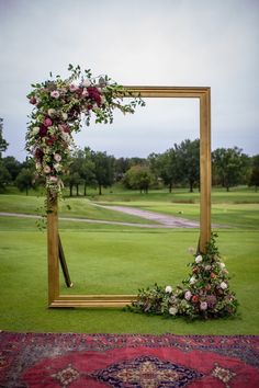 a wedding arch decorated with flowers and greenery on the grass near a golf course