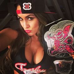 a beautiful woman wearing a black hat and holding two wrestling belts