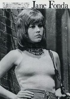 a woman in a white top is standing by a brick wall with her hands on her hips