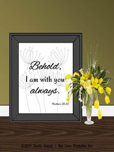 a vase filled with yellow flowers sitting next to a framed poster on top of a wooden table