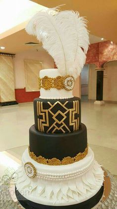 a three tiered cake with white feathers on top and gold trim around the edges