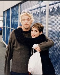 a man and woman standing next to each other near a fence with bags on their shoulders