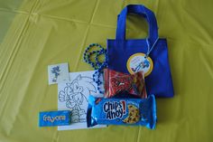 a blue bag filled with candy and other items sitting on top of a yellow table cloth