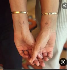 two people holding hands with cross tattoos on their wrist and fingers, both wearing gold bracelets