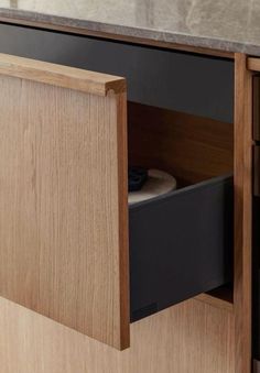 an open drawer in a wooden cabinet next to a marble counter top with black drawers