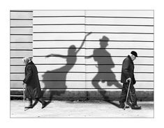 two people are walking down the street with their shadows on the wall and one is holding a cane