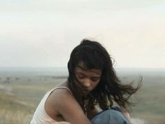 a woman with long hair sitting on top of a hill