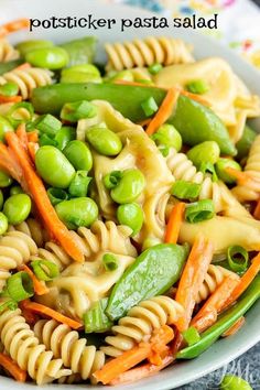 a pasta salad with peas, carrots and green peppers in a white bowl on a table