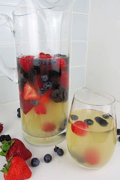 two glasses filled with liquid and fruit on the table next to each other, including strawberries, blueberries, and raspberries