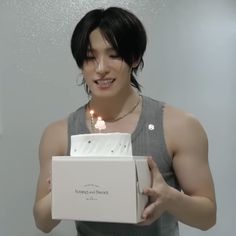 a young man holding a birthday cake with candles in it's box and smiling at the camera