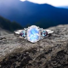 a white ring with blue and pink stones on top of a rock in the mountains