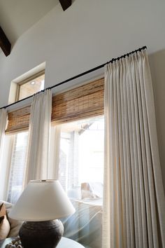 a lamp is sitting on a table in front of a window with white drapes