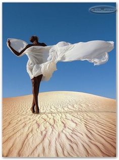 a woman standing on top of a sandy hill holding a white dress in her hand