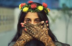 a woman with her hands on her face covered in hendix and flowers, covering her eyes