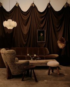 a living room with brown drapes and two chairs, a coffee table and ottoman