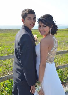 a man and woman standing next to each other in front of a fence on a field