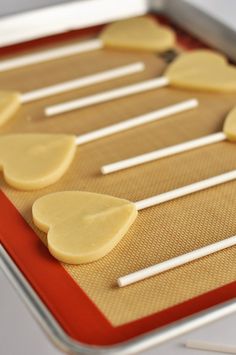 several pieces of heart shaped cookies on a cookie sheet with white sticks sticking out of them