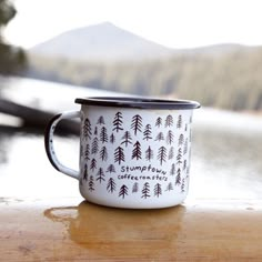 a white and black coffee cup sitting on top of a wooden table next to water