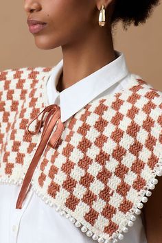 a woman wearing an orange and white crochet sweater with gold hoop earrings on her ear