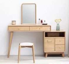 a wooden desk with a mirror, stool and flower vase on the table next to it