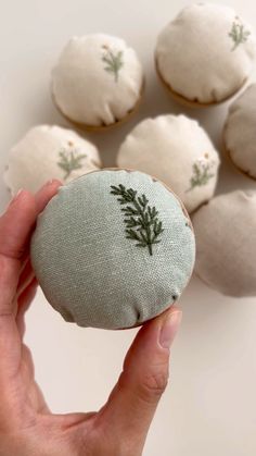 a hand is holding a small piece of fabric with green leaves on it and white background