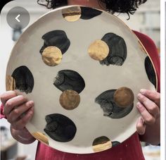 a woman holding a plate with black and gold circles on it