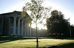 the sun shines brightly on an old building with columns and trees in the foreground