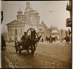 an old photo of people riding in a horse drawn carriage down the street with buildings behind them