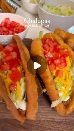 two hot dogs with toppings sit on a cutting board next to bowls of salad and condiments