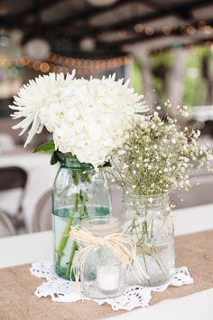 two mason jars filled with white flowers sitting on top of a table next to each other