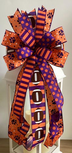 a purple and orange bow with footballs, paw prints and polka dots on it