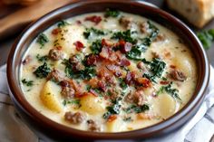 a bowl of soup with meat, cheese and spinach in it next to bread