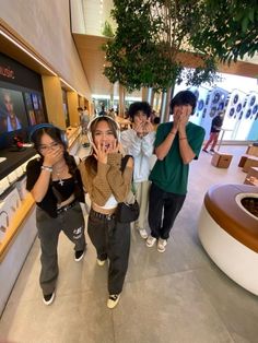 four people posing for a photo in front of a television screen at the mall with their hands up to their face