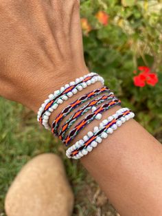 a woman's arm with several bracelets on it and flowers in the background