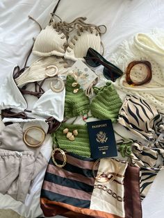 an assortment of clothing and accessories laid out on top of a white sheet with a passport