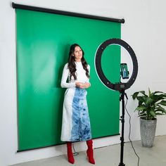 a woman standing in front of a green screen with a camera and light behind her