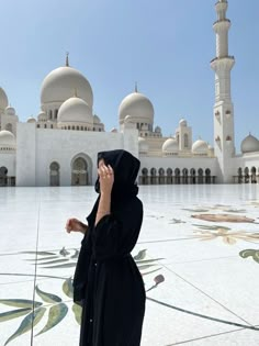 a woman standing in front of a building talking on a cell phone while wearing a hijab