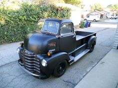 an old black truck is parked on the side of the road in front of some bushes