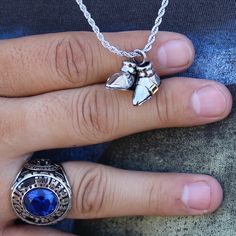 a person's hand holding a ring with a blue stone in the middle and a silver chain around it