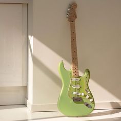 a green electric guitar sitting on the floor next to a white wall with sunlight streaming through it