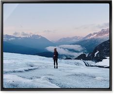 a woman standing on top of a snow covered slope with mountains in the back ground