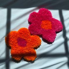 two orange and pink flowers sitting on top of a white sheet next to each other