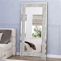 a large silver mirror sitting on top of a wooden floor next to a white bed