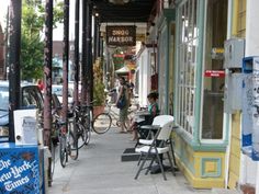 two people sitting at tables on the sidewalk in front of a barbershop and bike shop