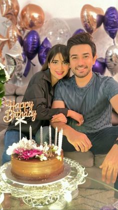 a man and woman sitting in front of a birthday cake