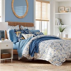 a bedroom with blue walls and floral bedding in the center, along with a round mirror on the wall