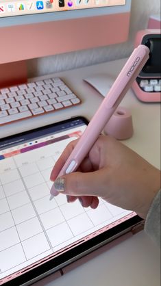 a person is holding a pencil in front of a computer keyboard and pad with a calendar on it