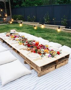 a long table is set up outside with food on it and lit candles in the background