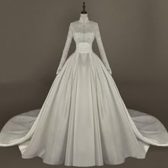 a white wedding dress with long sleeves and lace on the top, in front of a gray background