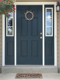 a blue front door with a wreath hanging on it's side and a welcome mat in front